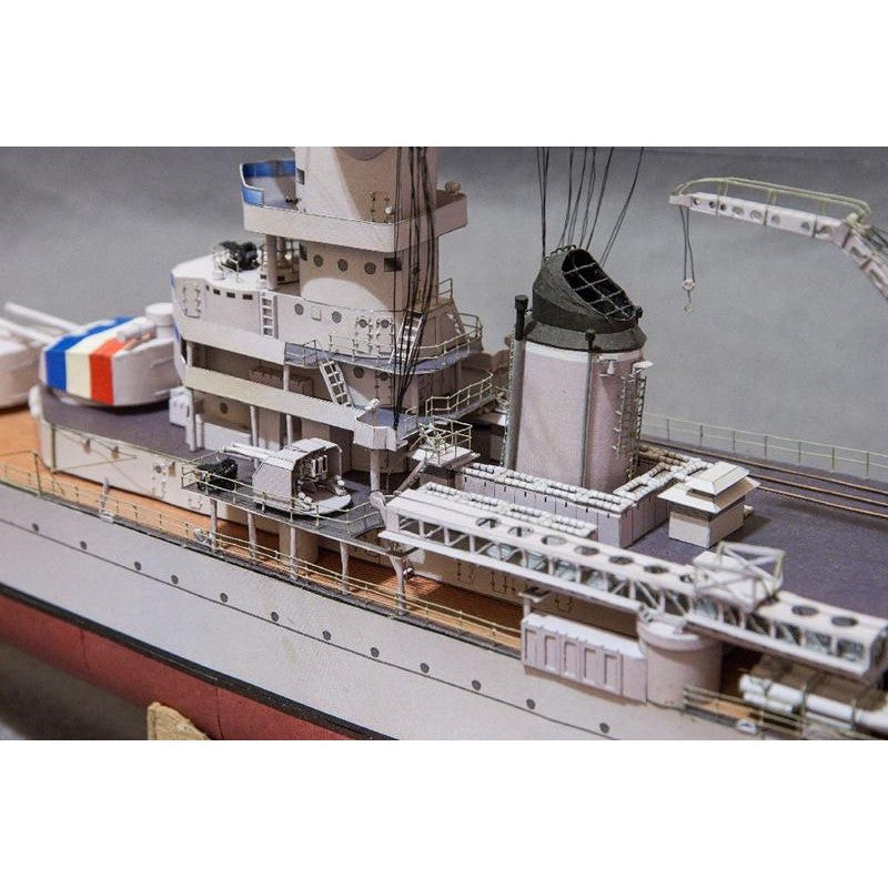 A close-up of a detailed model ship or boat deck, showing white and gray hull structures, a dark smokestack, deck equipment, and part of a red-and-white striped section on the side.