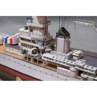 A close-up of a detailed model ship or boat deck, showing white and gray hull structures, a dark smokestack, deck equipment, and part of a red-and-white striped section on the side.