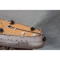 Close-up of a detailed model ship deck and hull, showing a beige wood-patterned deck, black chain, small black figures, and a white hull with the name ALGERIE printed on it.