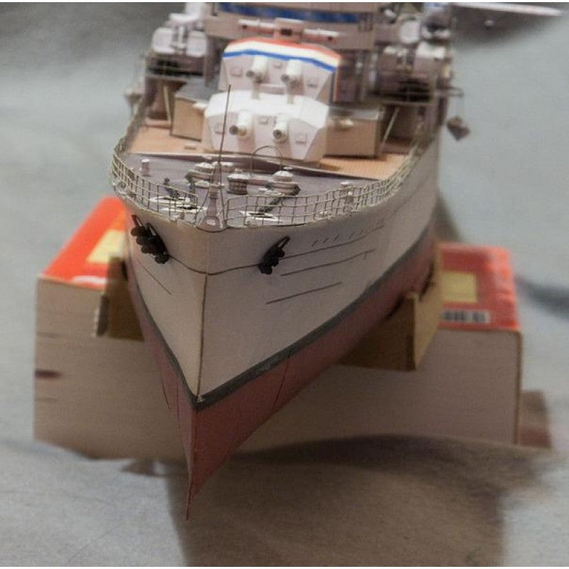 A close-up of a model ship or boat model photographed indoors, resting on small orange-and-white blocks against a gray surface.