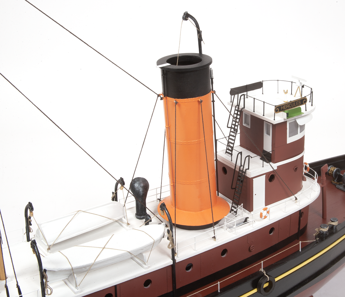 A detailed model of a tugboat, featuring a prominent orange and black smokestack, a white superstructure, and a dark red hull, photographed against a seamless white background.
