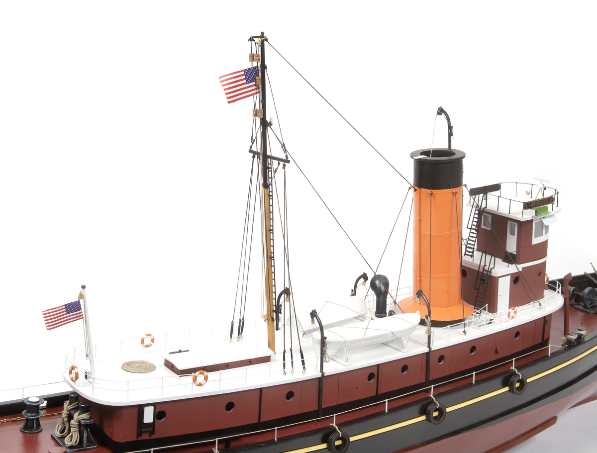 A detailed model of a tugboat, shown from a side angle against a plain white background. The boat features a dark reddish-brown hull, a white upper deck, a prominent orange smokestack, and black details including rigging, fenders, and an American flag flying from the mast.