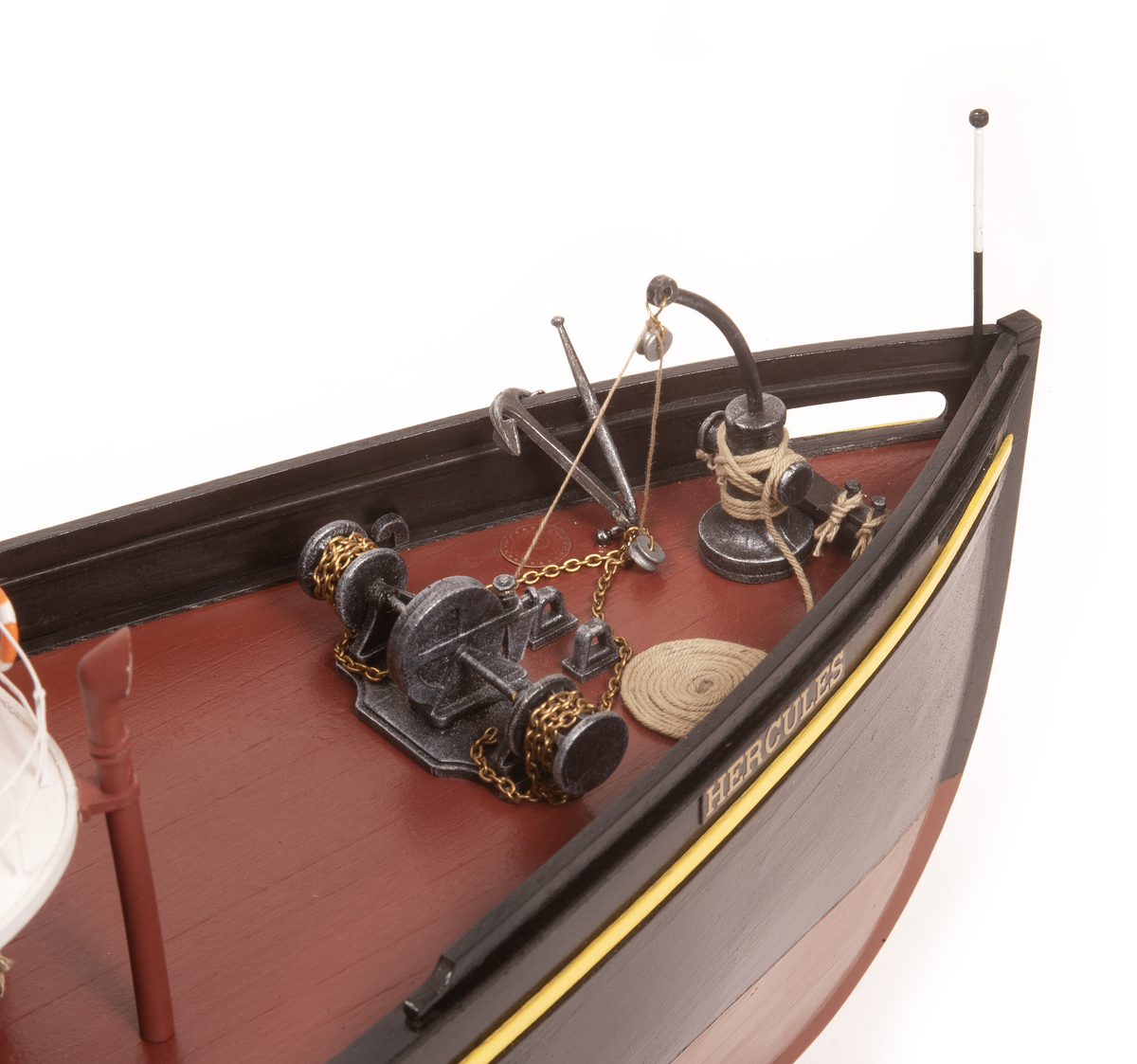 A close-up of a detailed model boat deck, featuring a reddish-brown wooden floor, black hull, brass and steel nautical equipment including an anchor, winch, and chains, and the name 'HERCULES' printed on the side.