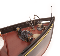 A close-up of a detailed model boat deck, featuring a reddish-brown wooden floor, black hull, brass and steel nautical equipment including an anchor, winch, and chains, and the name 'HERCULES' printed on the side.
