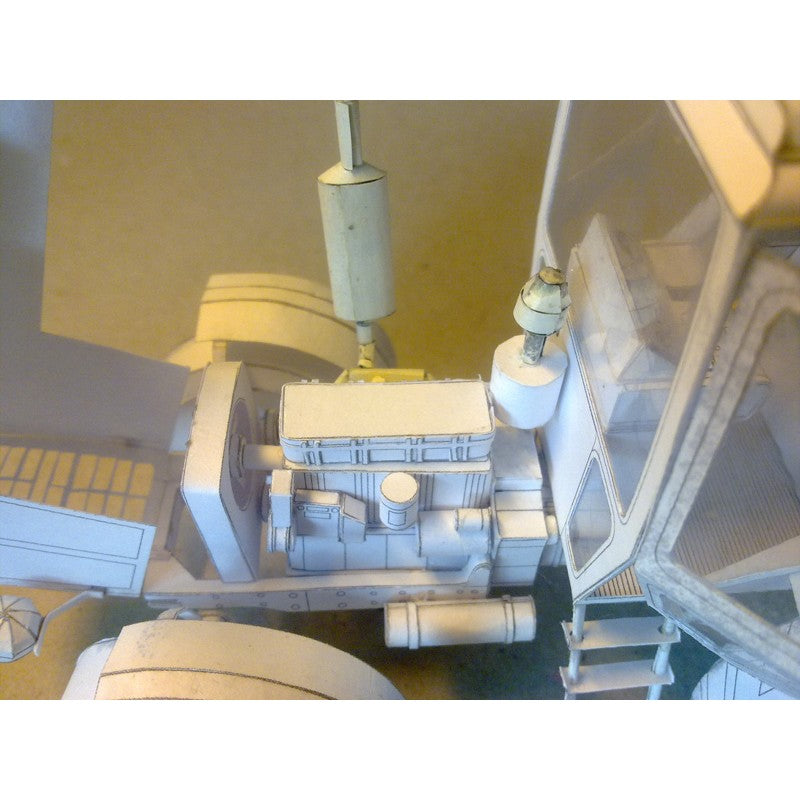 An unpainted white card model of a vehicle engine and chassis component, likely a scale model car or truck, photographed from a high-angle perspective.