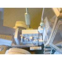 An unpainted white card model of a vehicle engine and chassis component, likely a scale model car or truck, photographed from a high-angle perspective.