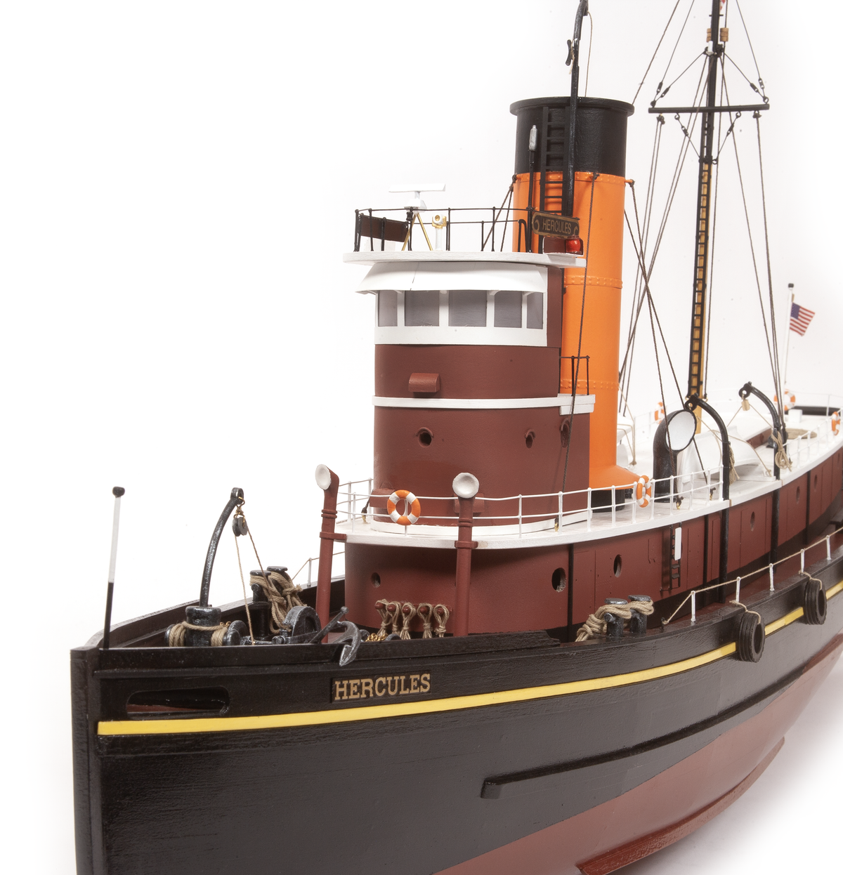 A detailed model of the tugboat Hercules, featuring a black hull, a dark red superstructure, and a bright orange smokestack, photographed against a seamless white background.