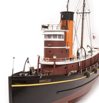 A detailed model of the tugboat Hercules, featuring a black hull, a dark red superstructure, and a bright orange smokestack, photographed against a seamless white background.
