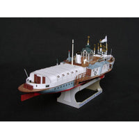 A detailed model of a passenger ship, likely a toy or scale model, displayed on a stand against a solid black background. The ship features a white upper deck, a light blue hull, brown wooden-style decks and railings, and small gold accents on the antennas and masts.