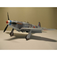A model of a Soviet fighter plane, likely a MiG-15, painted in a gray camouflage scheme with red star insignias, orange text, and a blue and red nose cone, displayed on a neutral beige background.