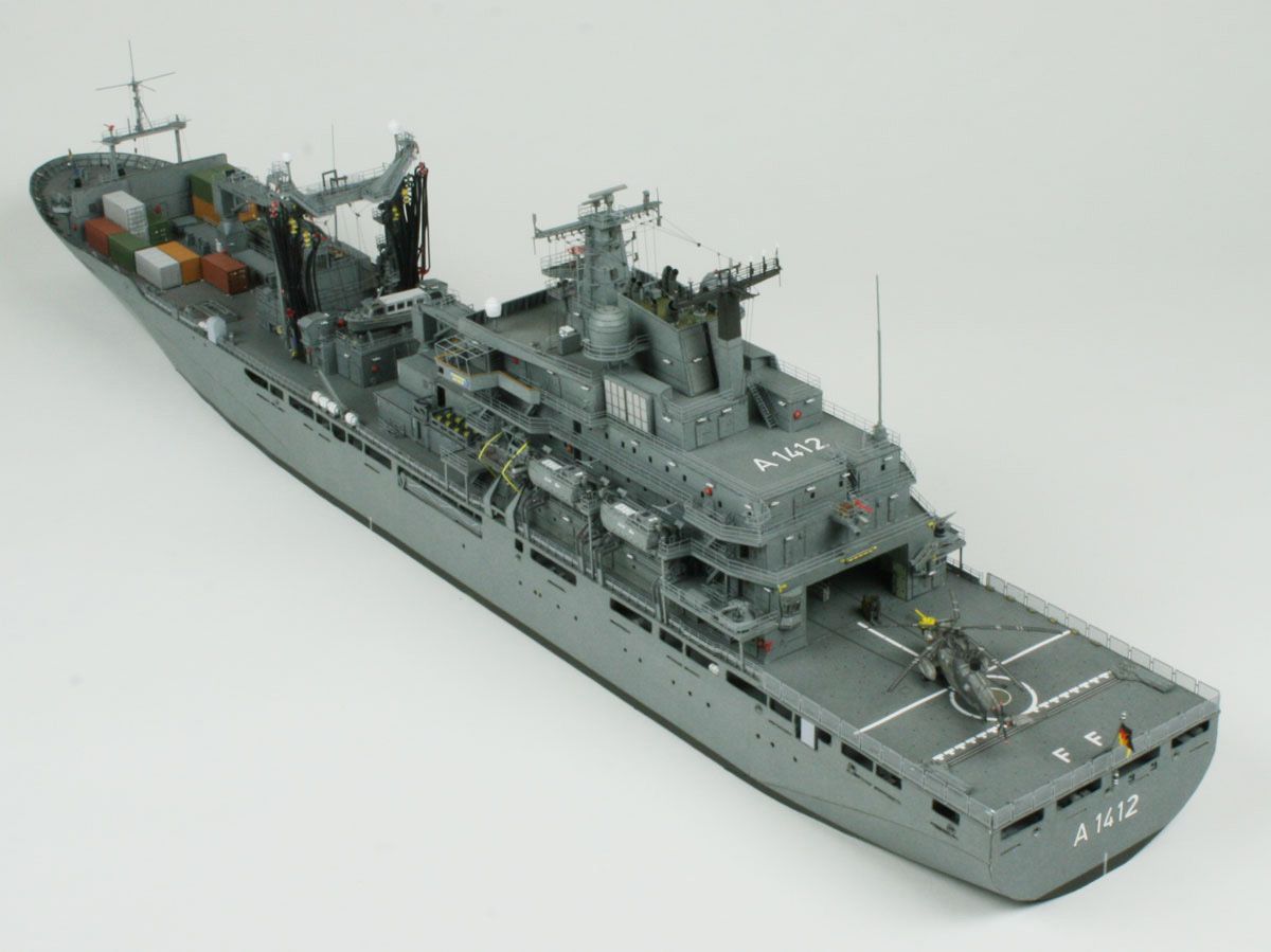 A detailed model of a gray military cargo ship, shown from an elevated three-quarters perspective against a seamless light gray background.