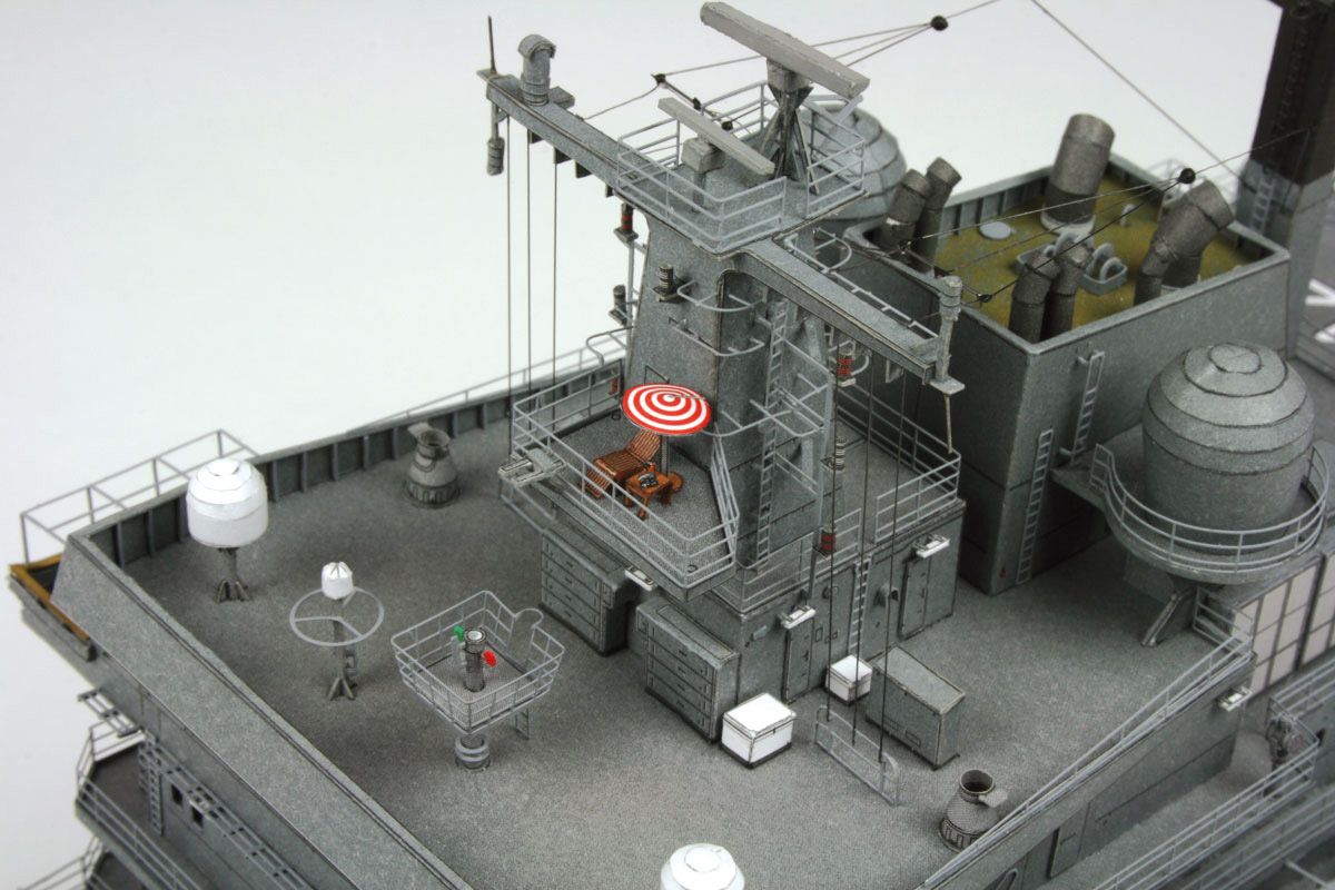 A detailed model of a gray military ship deck, featuring various antennas, radar domes, communication equipment, and small crew stations, photographed against a plain light gray background.