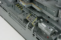 Close-up detail of a gray model ship or vessel deck with multiple decks, railings, yellow accents, and a large cylindrical structure labeled 'UKHO'.