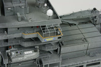 Close-up detail of a gray military ship model or miniature, showing decks, stairways, antennas, and a small lifeboat with DRKB markings.