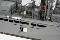 Close-up detail of a gray military ship deck with antennas, equipment, railings, and a small yellow forklift model.