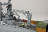 A detailed model of a cargo ship deck featuring a gray gantry crane, stacked shipping containers in green, orange, and white, and a gray superstructure, set against a plain light gray background.