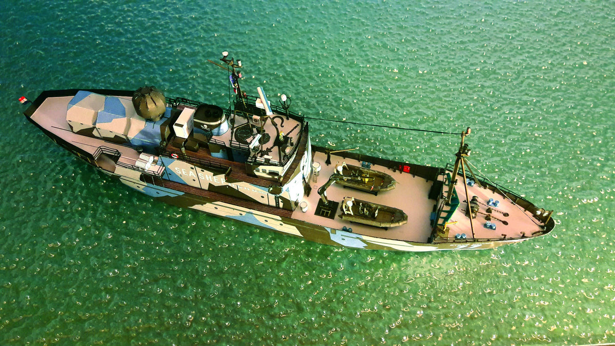 An aerial view of a camouflage-patterned fishing boat floating on clear turquoise water.
