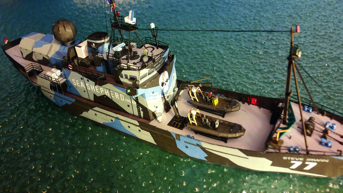 A small model fishing vessel named 'Steve Sawyer 77' painted in a blue, gray, and brown camouflage pattern, floating on green-blue water.