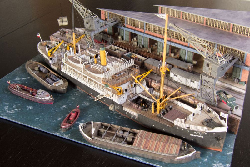 Photo of Harbor Diorama Hamburg 1:250 card model kit by HMV showing the weathered steamer Schwan and detailed 1930s harbor scene with cranes, vehicles, and warehouse.