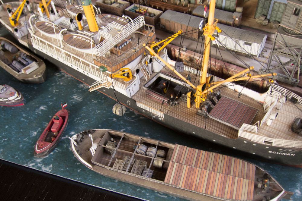 Photo of Harbor Diorama Hamburg 1:250 card model kit by HMV showing the weathered steamer Schwan and detailed 1930s harbor scene with cranes, vehicles, and warehouse.