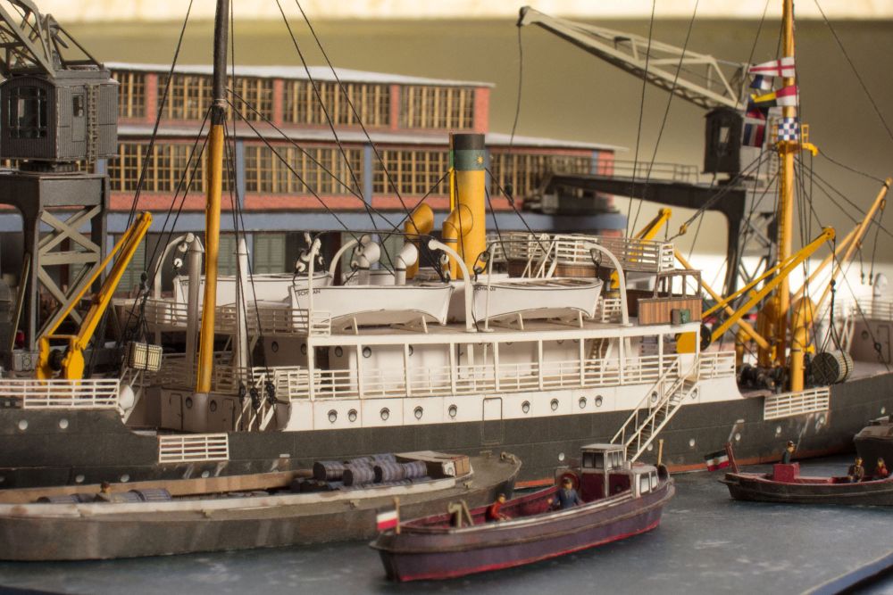 Photo of Harbor Diorama Hamburg 1:250 card model kit by HMV showing the weathered steamer Schwan and detailed 1930s harbor scene with cranes, vehicles, and warehouse.