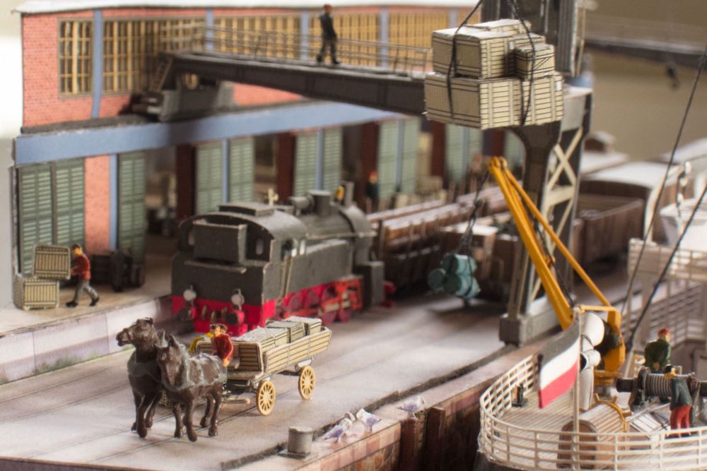 Photo of Harbor Diorama Hamburg 1:250 card model kit by HMV showing the weathered steamer Schwan and detailed 1930s harbor scene with cranes, vehicles, and warehouse.