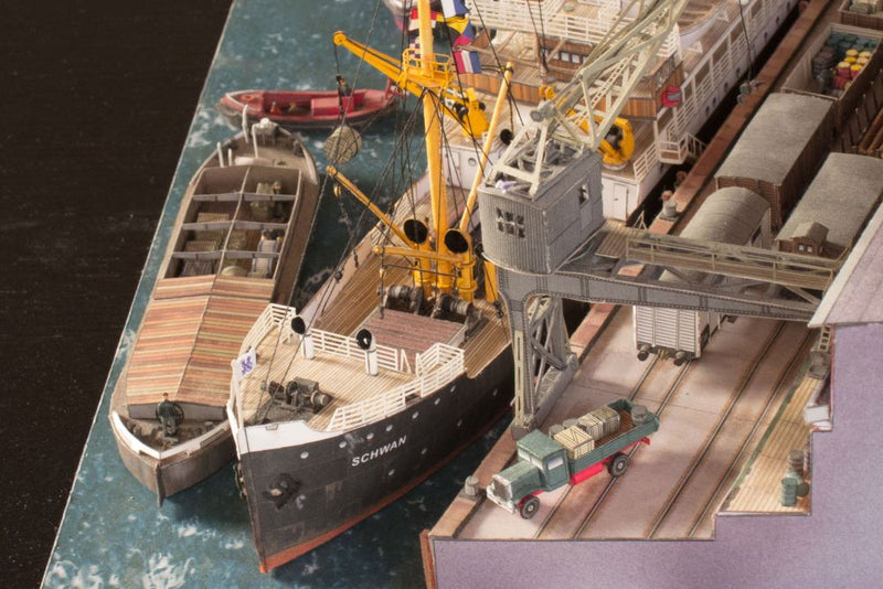 Photo of Harbor Diorama Hamburg 1:250 card model kit by HMV showing the weathered steamer Schwan and detailed 1930s harbor scene with cranes, vehicles, and warehouse.
