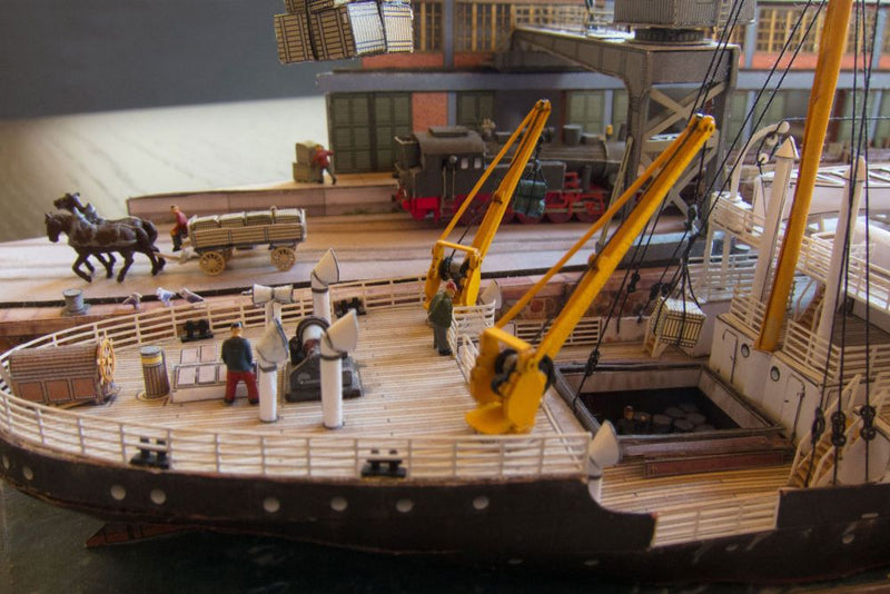Photo of Harbor Diorama Hamburg 1:250 card model kit by HMV showing the weathered steamer Schwan and detailed 1930s harbor scene with cranes, vehicles, and warehouse.