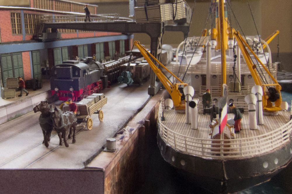 Photo of Harbor Diorama Hamburg 1:250 card model kit by HMV showing the weathered steamer Schwan and detailed 1930s harbor scene with cranes, vehicles, and warehouse.