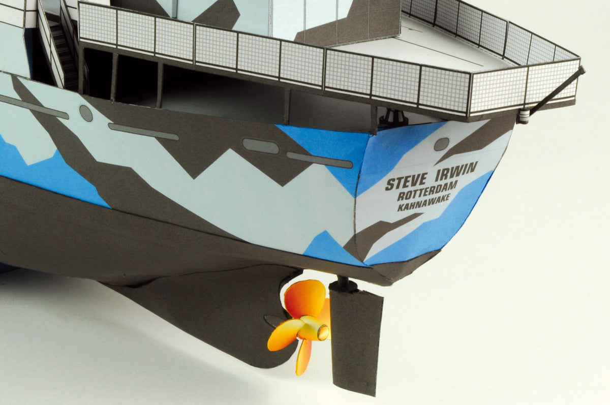 A close-up of a model boat or ship hull with a dark gray and light blue camouflage pattern, featuring the text 'STEVE IRWIN' and 'ROTTERDAM KANAROWA' on the side, plus an orange-and-yellow propeller at the bottom.