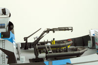 A miniature model of a ferry deck featuring a black and yellow rigid airboat, a black crane, and a white and blue ferry superstructure, set against a plain off-white background.