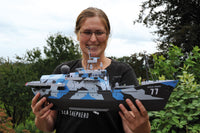 A woman outdoors holding a detailed model of a military ship named 'Sea Shepherd' with the number 77 on its hull.