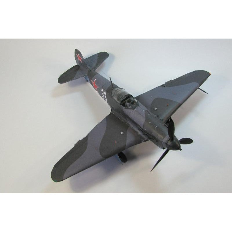A model of a World War II fighter plane, likely a Soviet aircraft, painted in a dark gray and black camouflage pattern with red star insignias on the tail and fuselage, photographed on a light gray background.