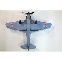 A model or miniature of a Soviet military jet aircraft, viewed from directly underneath. The plane is painted in a light blue-gray color with red five-pointed star insignias on the wings, set against a plain off-white background.