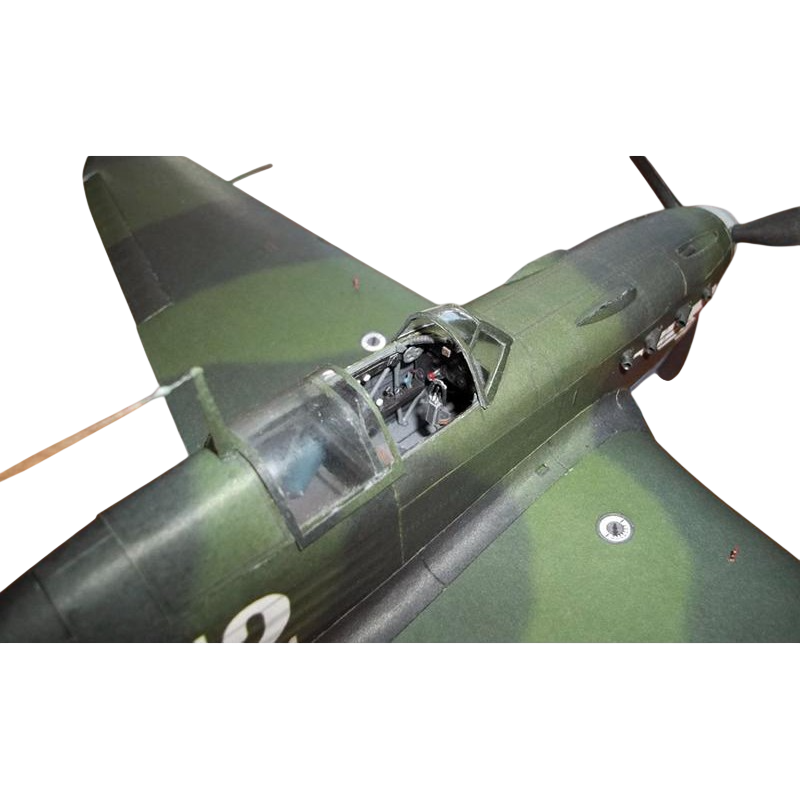 Close-up of a model or miniature military airplane, showing part of the wing, fuselage, cockpit, and propeller against a plain white background.