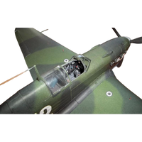 Close-up of a model or miniature military airplane, showing part of the wing, fuselage, cockpit, and propeller against a plain white background.
