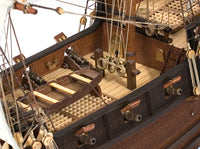 Photo of OcCre Buccaneer Pirate Ship 1:100 Wooden Model Kit fully assembled, showing detailed sails, wooden hull, and rigging.