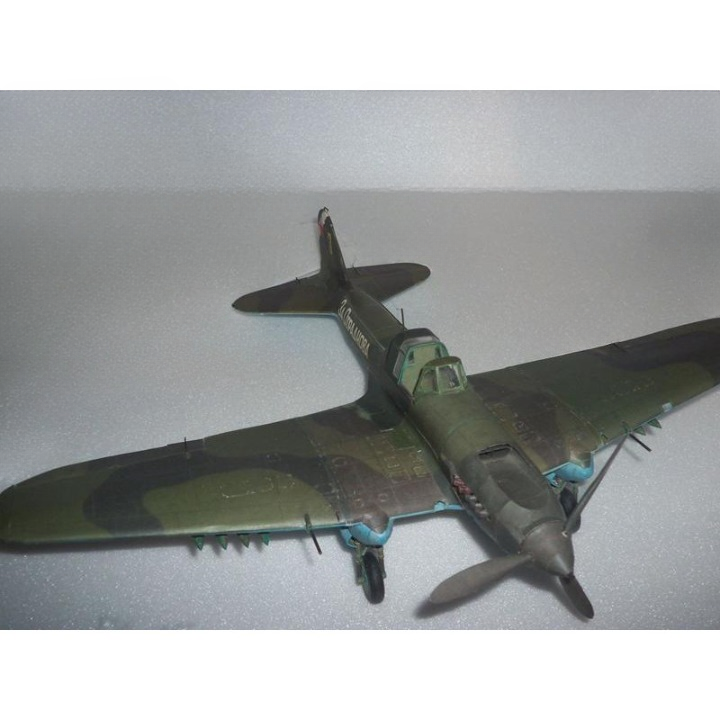 A vintage military model airplane with a green camouflage pattern, photographed on a light gray textured surface.