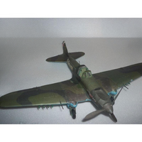 A vintage military model airplane with a green camouflage pattern, photographed on a light gray textured surface.