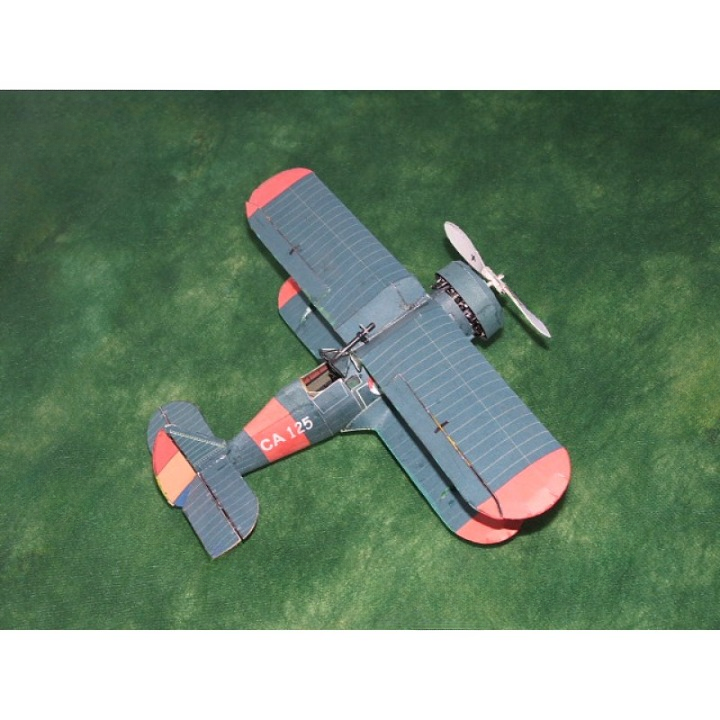 A small model biplane with a blue-gray fuselage and wings, red wingtips, and orange-red tail sections, photographed on a green textured surface.