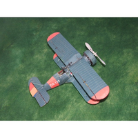 A small model biplane with a blue-gray fuselage and wings, red wingtips, and orange-red tail sections, photographed on a green textured surface.