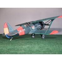 A vintage-style biplane model aircraft with a dark teal-blue body, red wingtips and tail section, and cream accents, displayed on a green textured surface against a plain gray background.