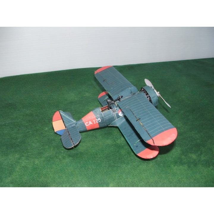 A small wooden biplane model with a dark blue-gray body, red wingtips and tail tips, and orange accents on the tail, displayed on a green textured surface against a white background.