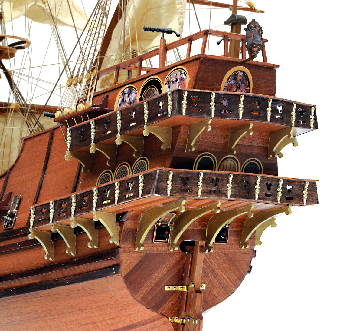 Close-up of a detailed wooden pirate ship model, showing the ornate multi-decked hull, decorative railings, brass cannons, and cream-colored sails against a plain white background.