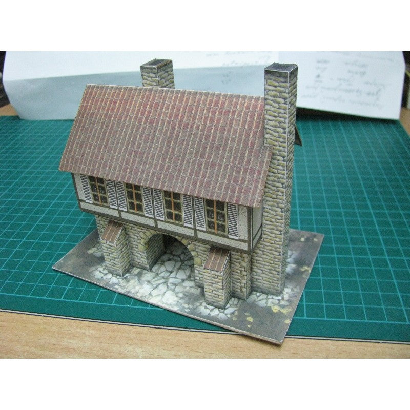 A miniature model of a stone house with a brown tiled roof, set on a green cutting mat.