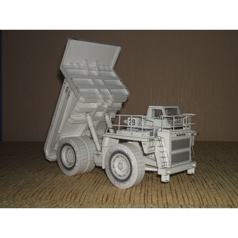 A detailed miniature model of a white dump truck with its bed raised, displayed on a textured beige surface against a brown backdrop.