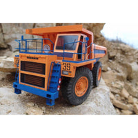 An orange and blue toy mining dump truck with the number 39, positioned on a rocky, outdoor-looking background.