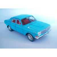 A turquoise blue vintage sedan model car with red interior windows, shown from a three-quarter front angle on a light blue studio background.