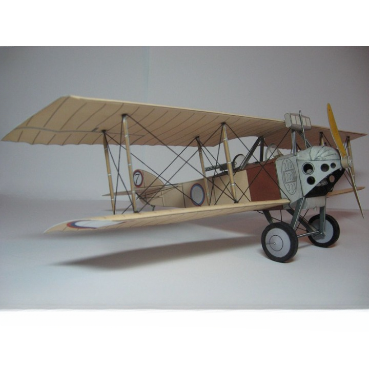 A vintage-style biplane model or miniature aircraft shown in side profile against a plain light gray studio background. The plane has a cream/beige wing structure, dark struts, a white fuselage with black details, a brown side panel, and small roundel markings on the wings.