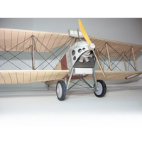 A vintage-style biplane model with a silver fuselage, cream-colored wooden wings, black wire struts, gray wheels, and a yellow propeller, photographed against a plain light gray background.